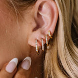 Close-up of an ear wearing gold hoop earrings with a hand adjusting them.