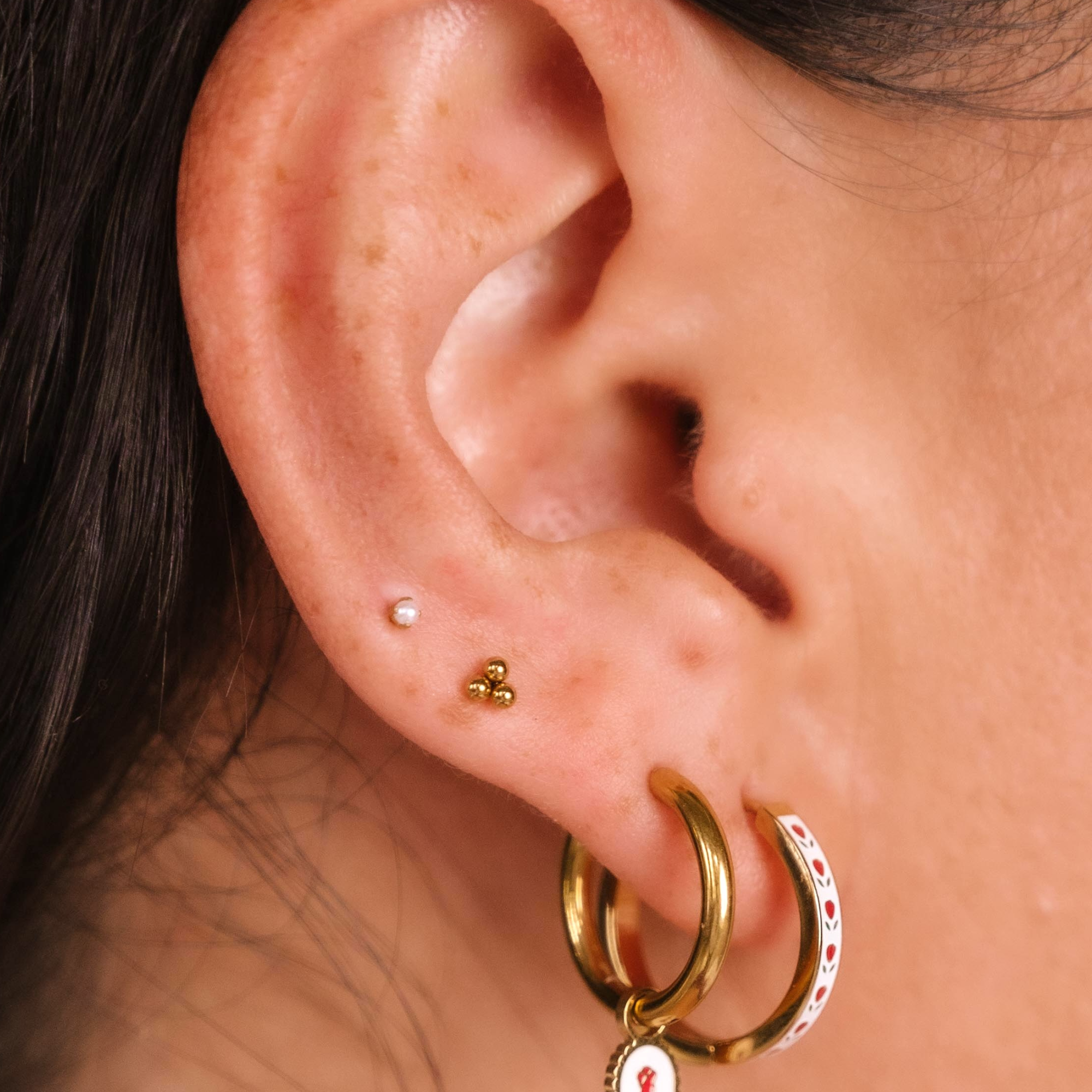 Close-up of an ear wearing gold hoop earrings with floral charms.