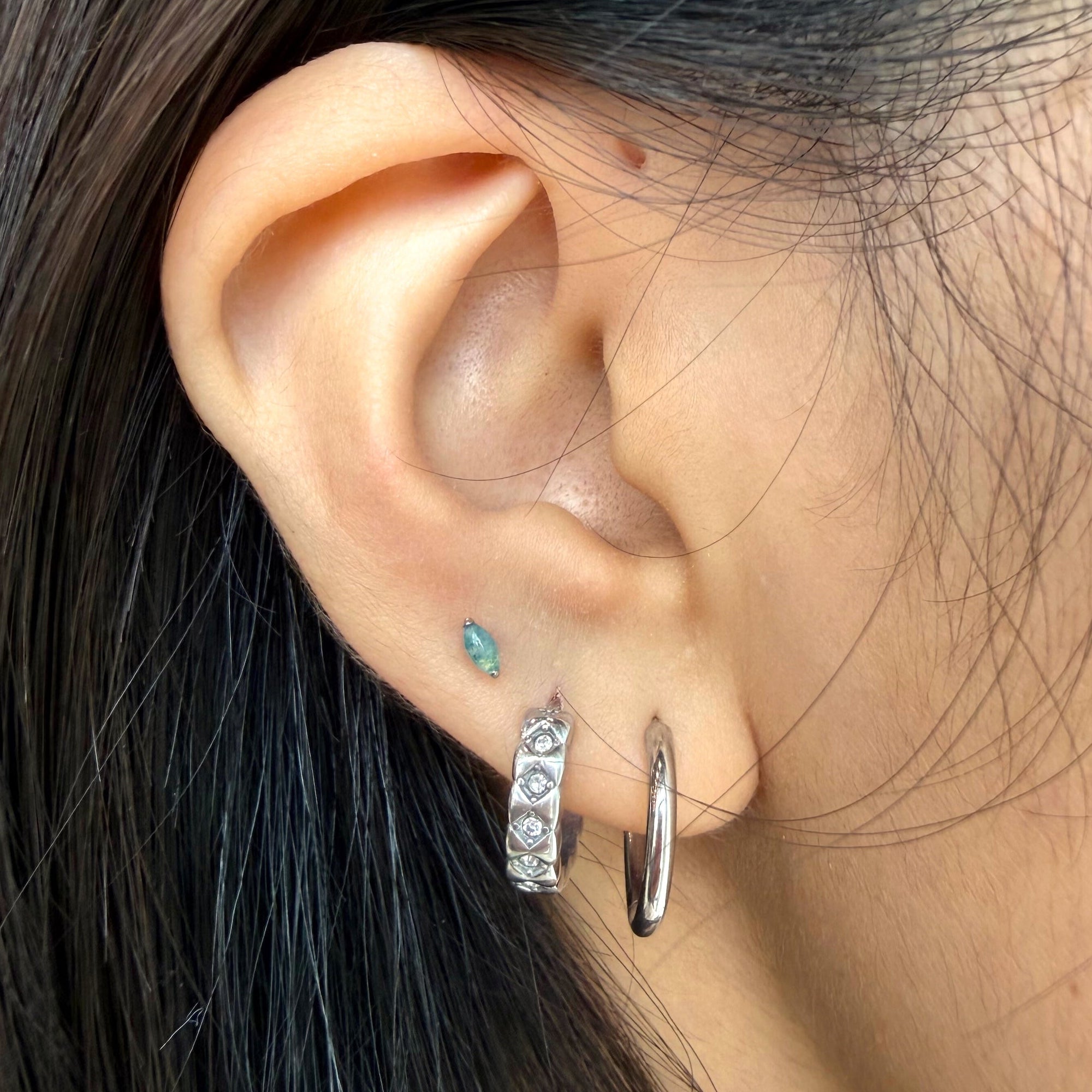Close-up of an ear with multiple earrings against a blurred background