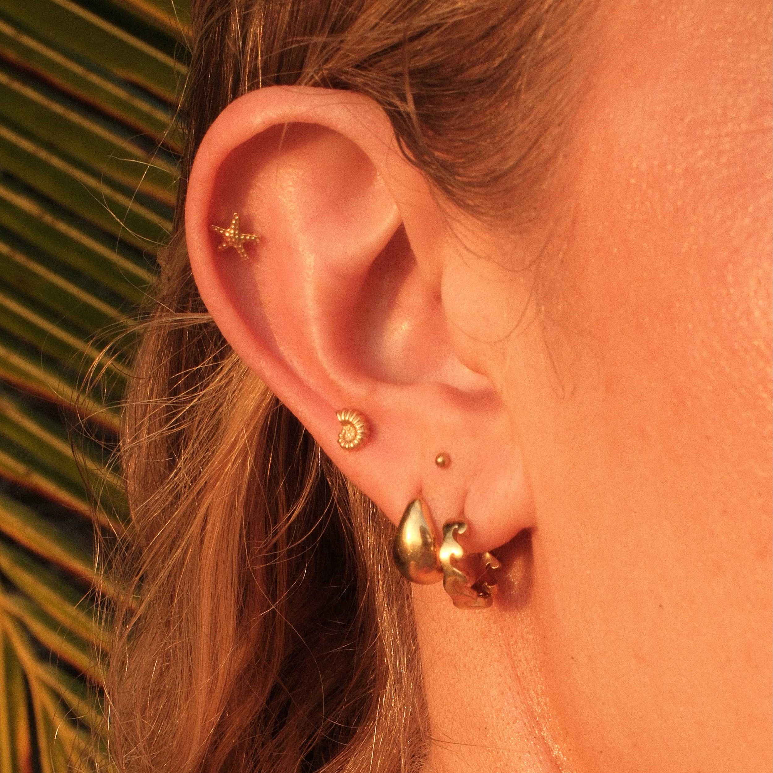 Close-up of an ear with gold earrings against a blurred natural background