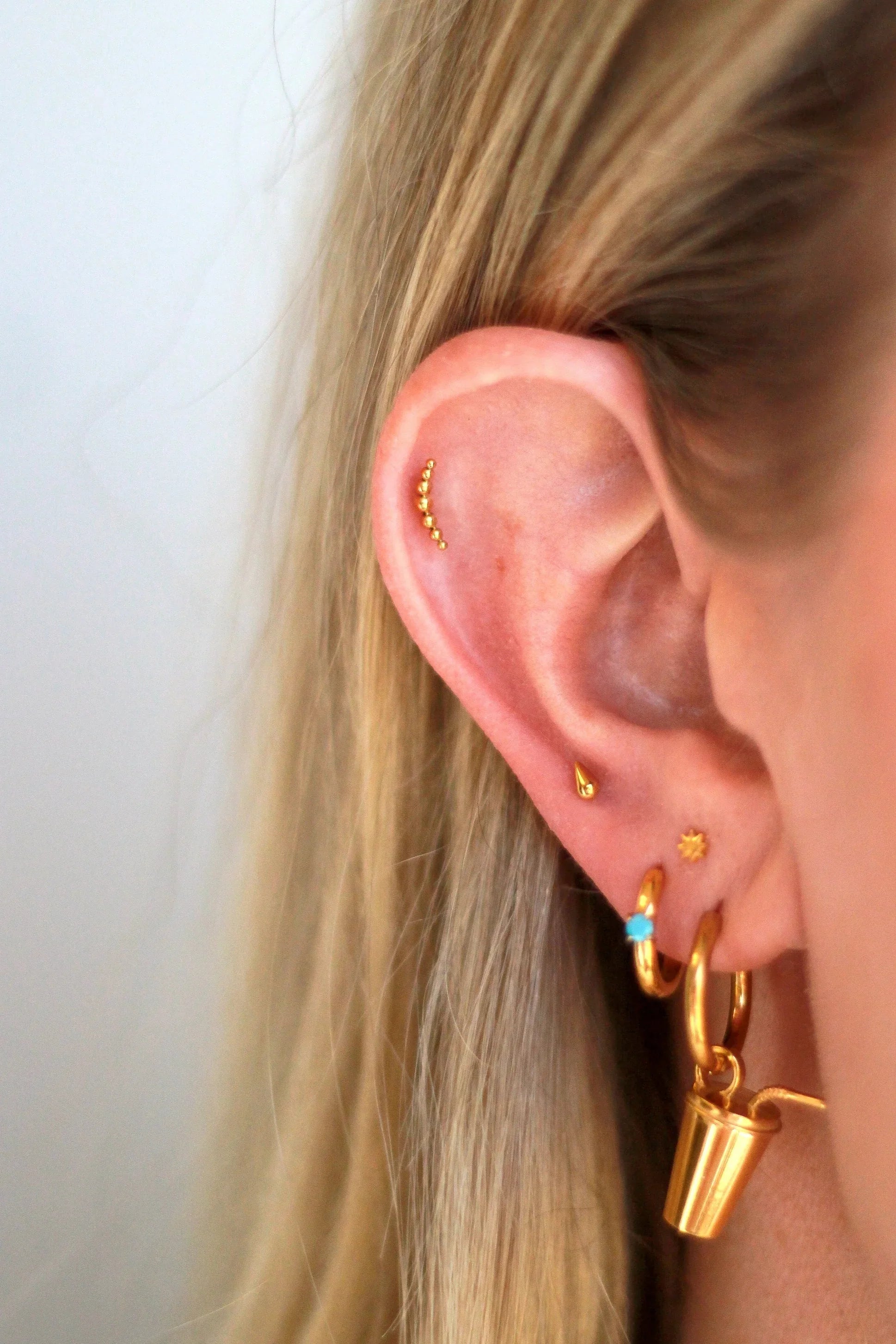 Close-up of an ear wearing gold hoop earrings with a plain background