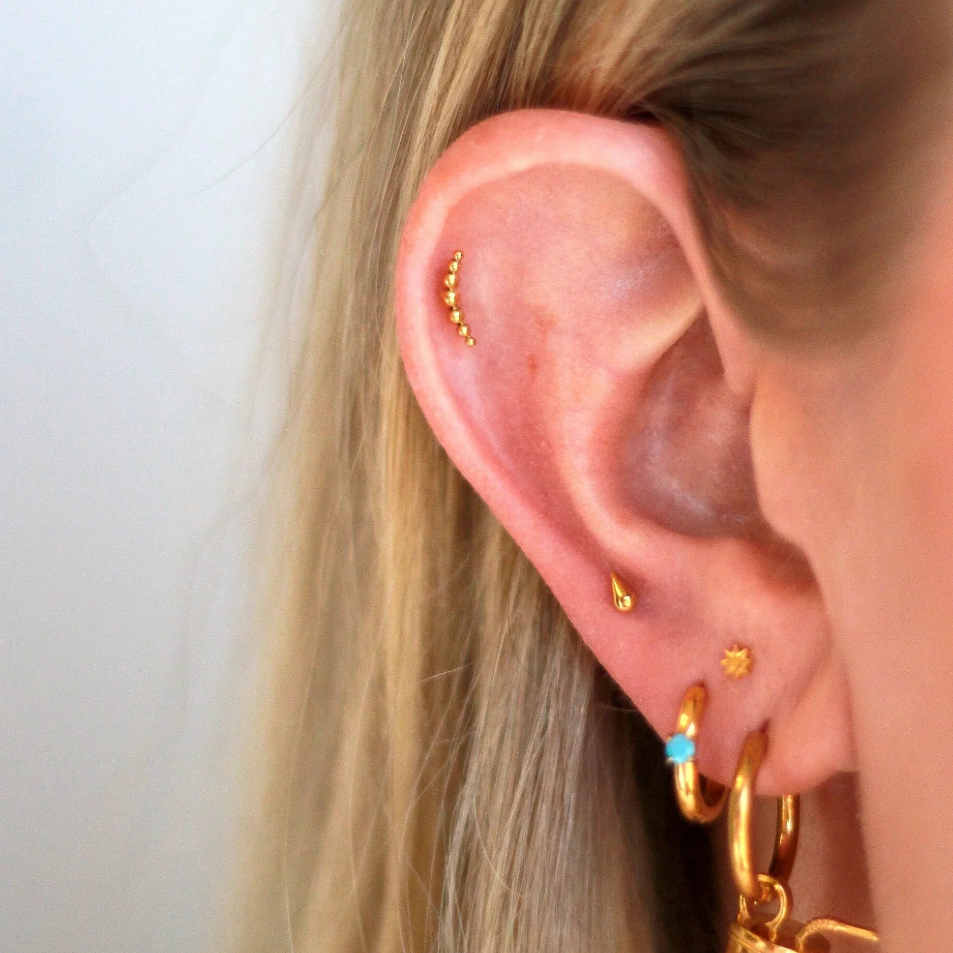 Close-up of an ear wearing gold hoop earrings with a plain background