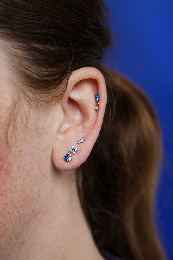 Close-up of an ear with multiple earrings against a blue background
