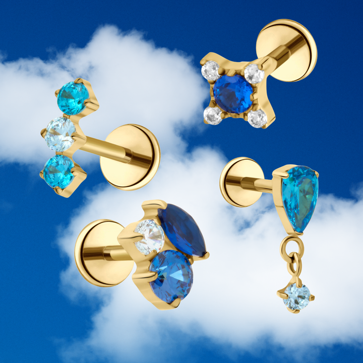 Gold flat back stud earrings with blue and turquoise gemstones against a blue sky background
