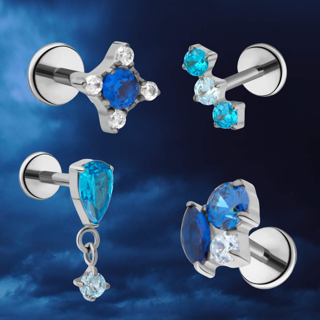 Set of titanium flat back stud earrings with blue CZ gemstones on a dark blue sky background