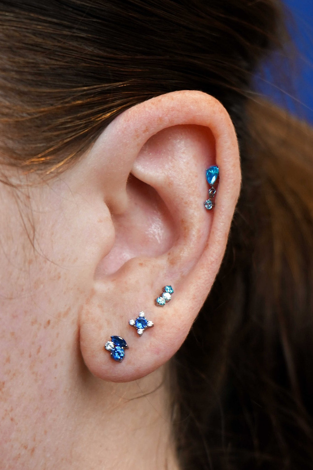 Close-up of an ear with multiple blue gemstone earrings.