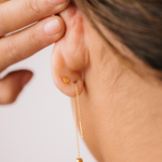 Close-up of a person wearing a gold threader earring with a hand adjusting it on a light background