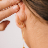 Close-up of a person wearing a gold threader earring with a hand adjusting it on a light background