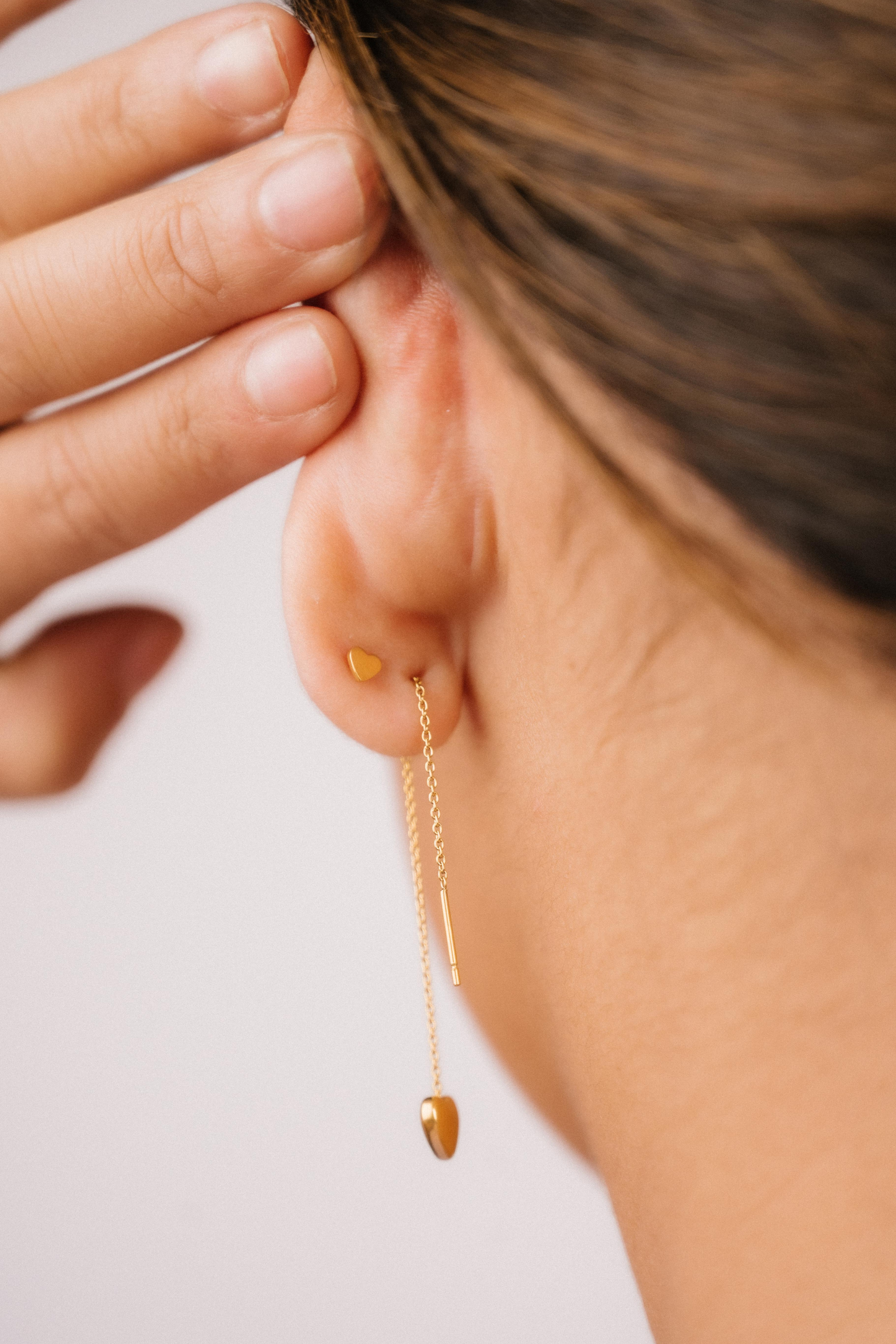 Close-up of a person wearing a gold threader earring with a hand adjusting it on a light background