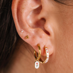 Close-up of an ear wearing gold hoop earrings with floral designs.