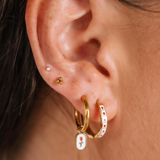 Close-up of an ear wearing gold hoop earrings with floral designs.