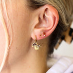 Gold earrings with a small pendant worn by a person with blonde hair.
