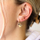 Gold earrings with a small pendant worn by a person with blonde hair.