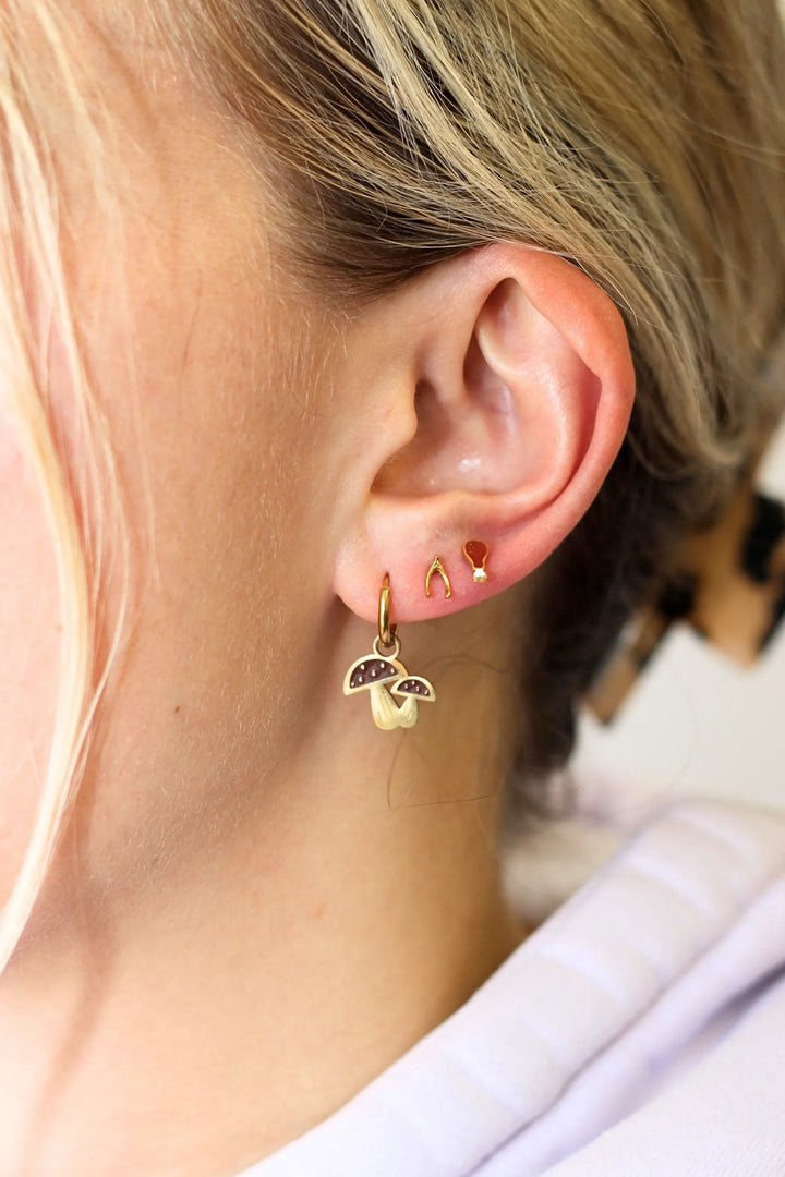 Gold earrings with a small pendant worn by a person with blonde hair.
