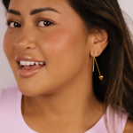 Woman wearing gold heart threader earrings with a white background