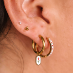 Close-up of an ear with gold hoop earrings featuring floral charms.