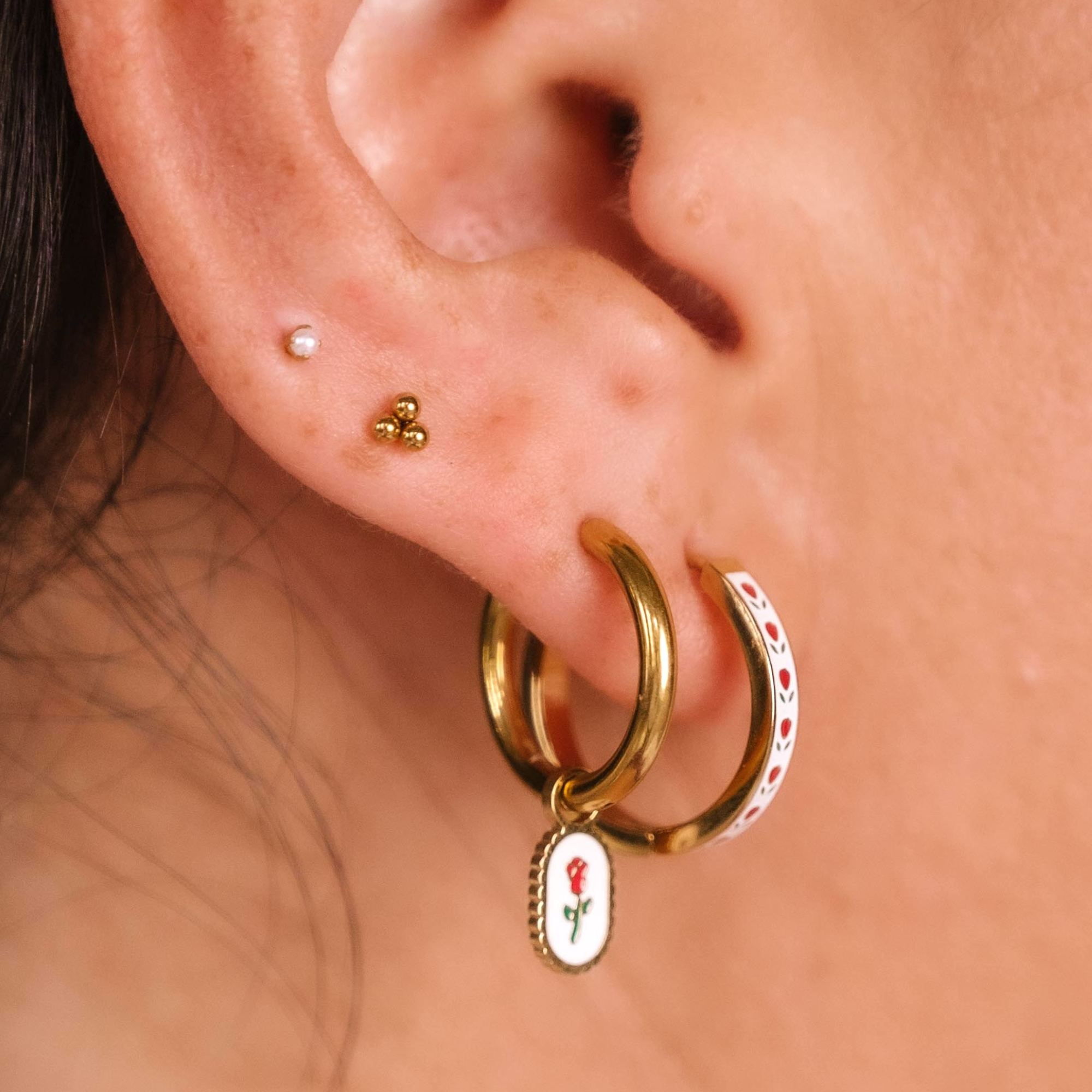 Close-up of an ear with gold hoop earrings featuring floral charms.
