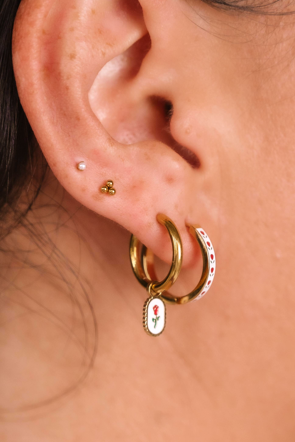 Close-up of an ear with gold hoop earrings featuring floral charms.