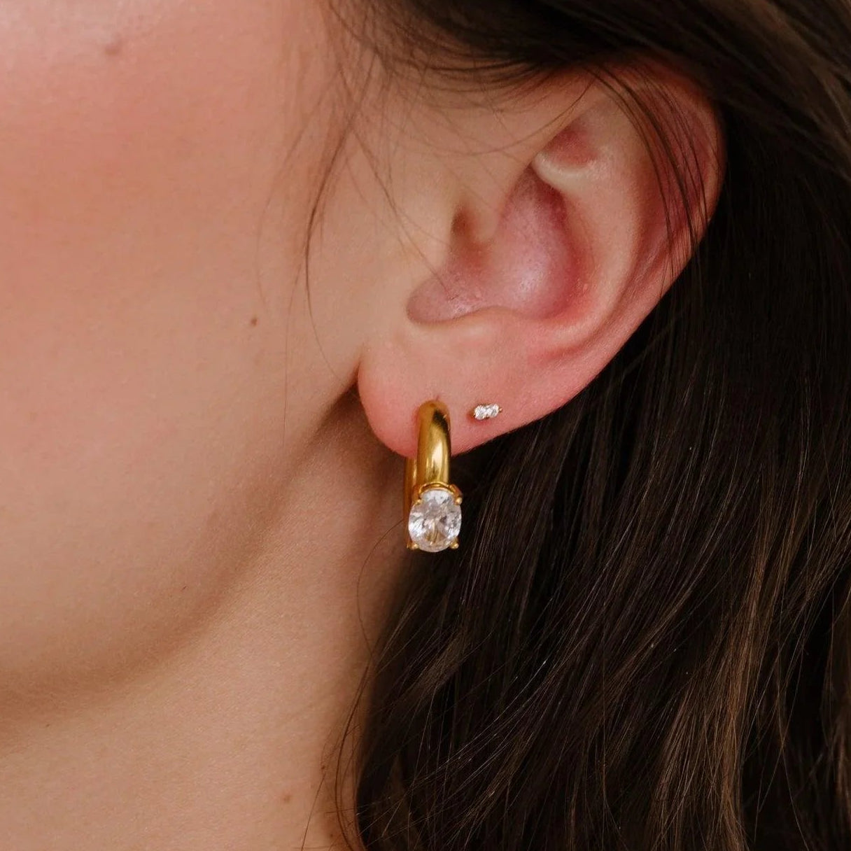 Close-up of a person wearing gold necklaces and earrings with a neutral background
