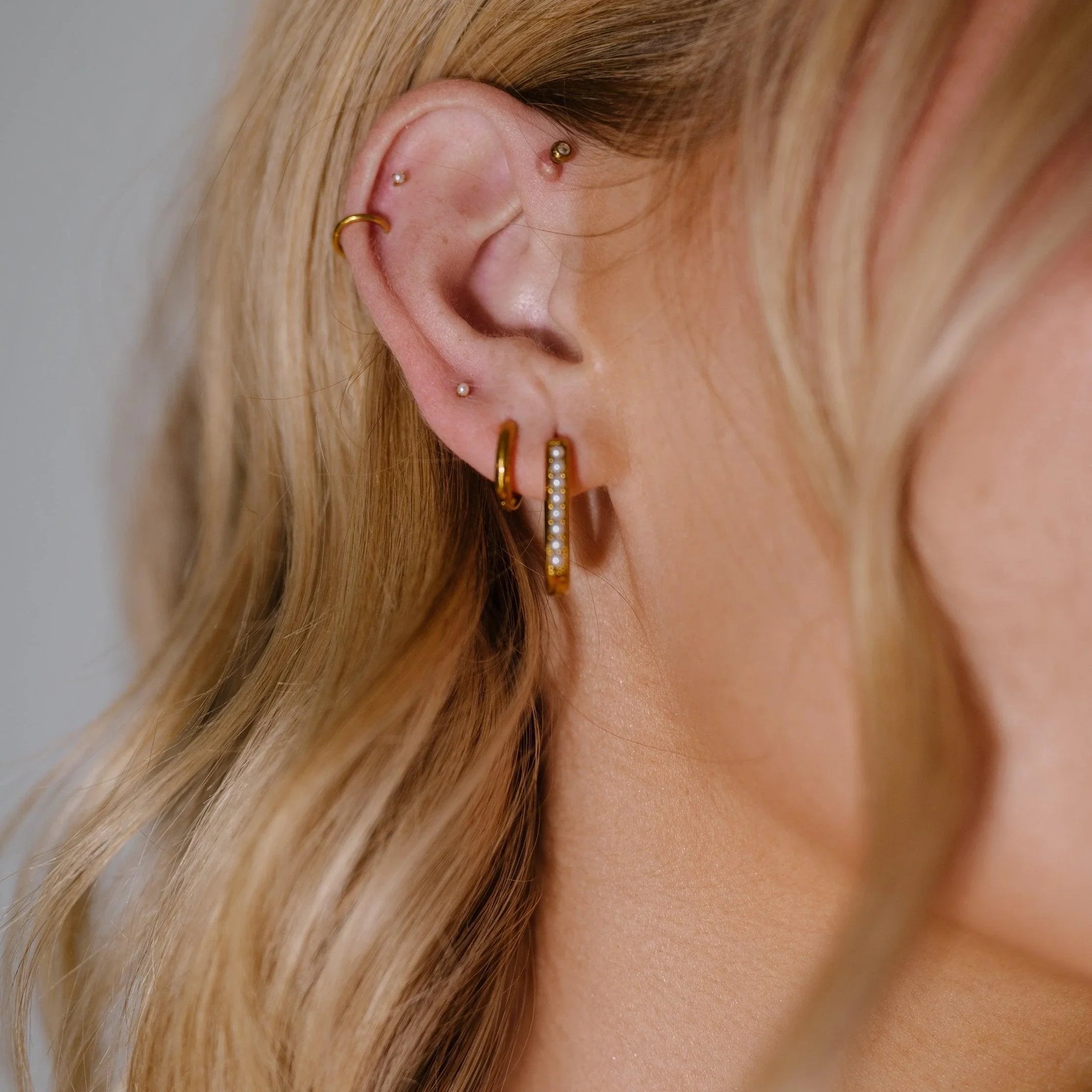 Close-up of a person's ear with gold hoop earrings against a neutral background