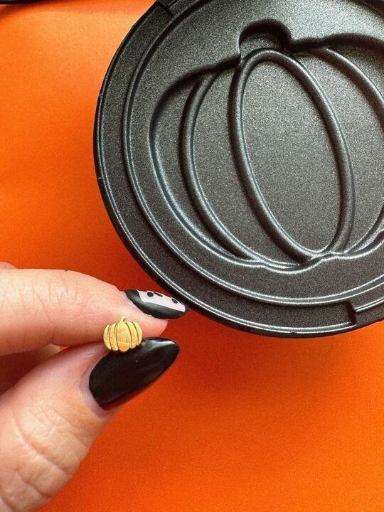 Hand holding a gold pumpkin-shaped stud earring next to an open pumpkin-shaped waffle iron.