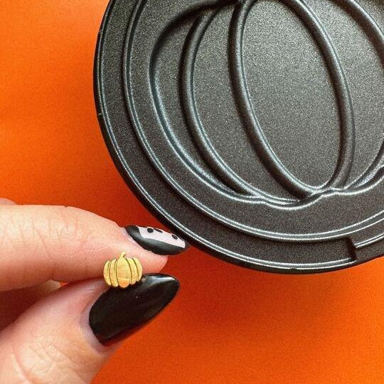 Hand holding a gold pumpkin-shaped stud earring next to an open pumpkin-shaped waffle iron.