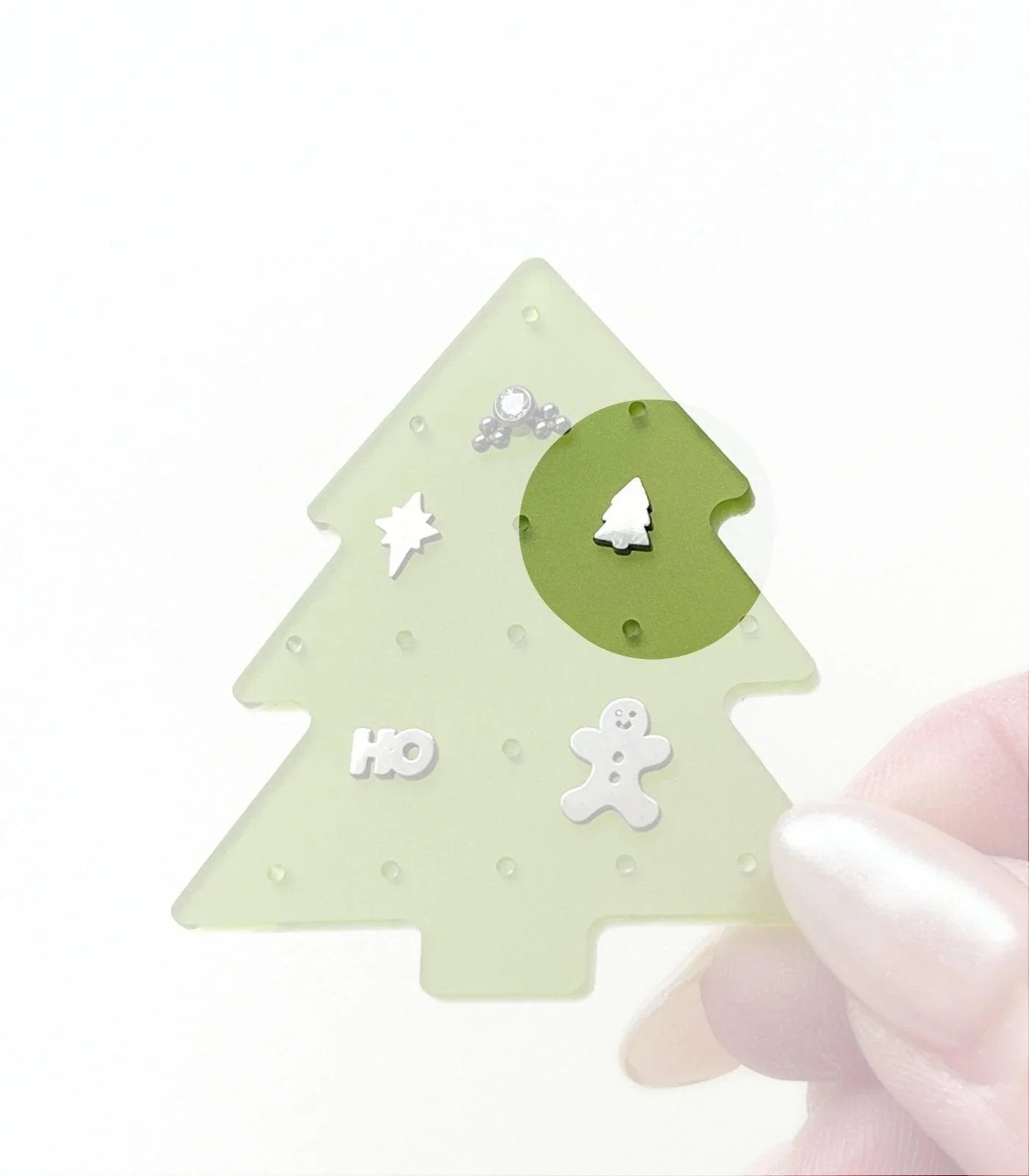 Christmas tree-shaped jewelry organizer with various silver small holiday-themed flat back studs, on a white background