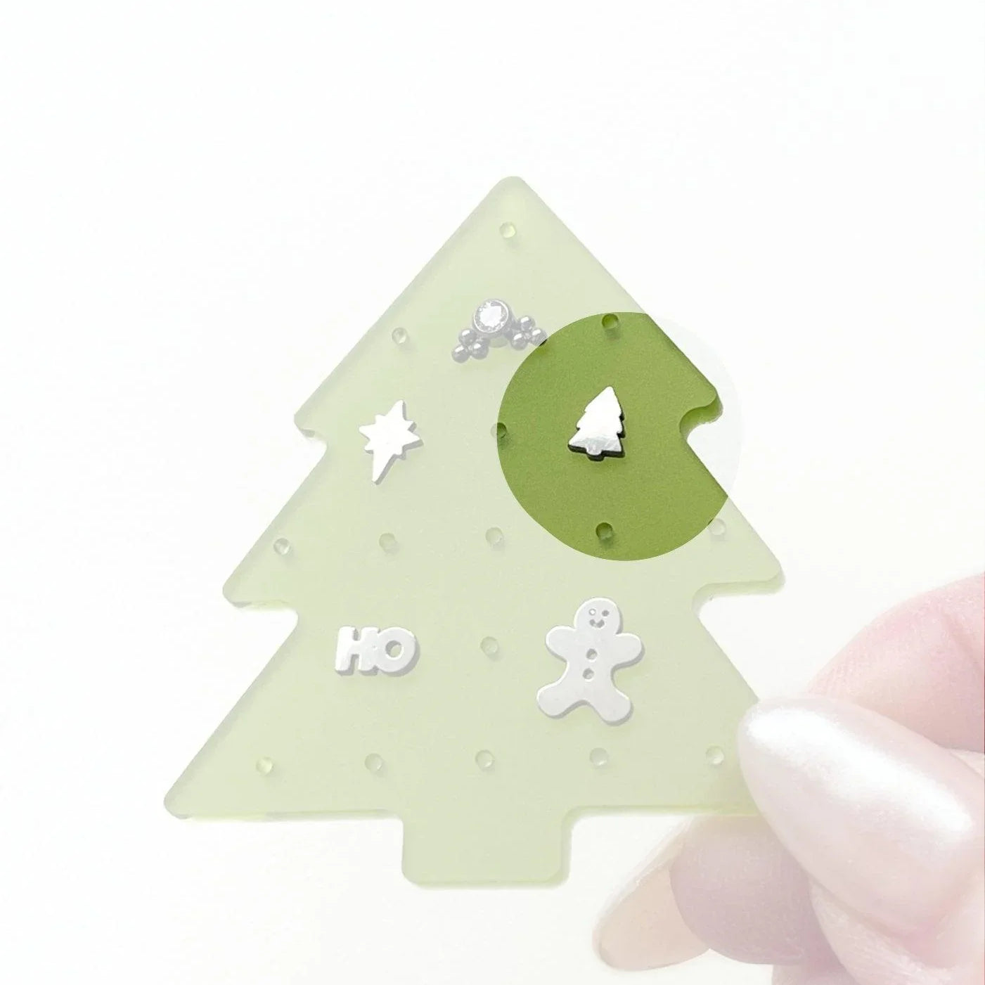 Christmas tree-shaped jewelry organizer with various silver small holiday-themed flat back studs, on a white background