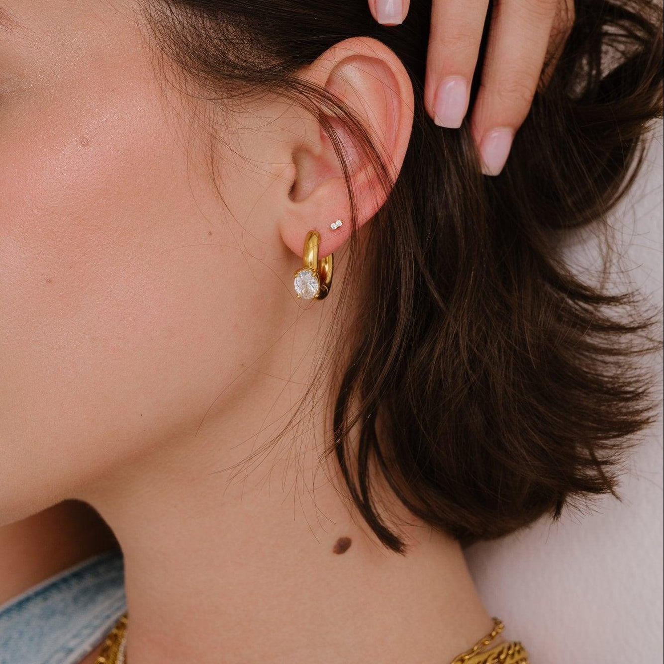 Woman wearing gold necklaces and earrings with a close-up of her ear.