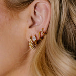 Close-up of a person wearing gold hoop earrings with a blurred background