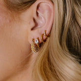 Close-up of a person wearing gold hoop earrings with a blurred background