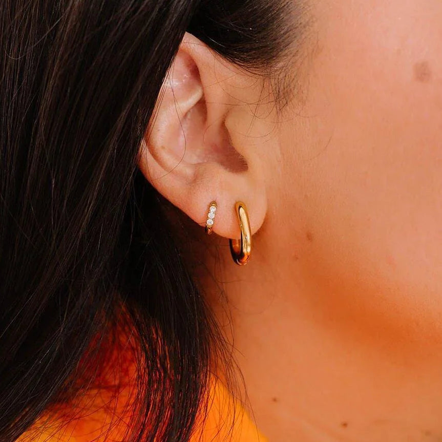 Close up of an ear with 2 styles of gold hoops on it.