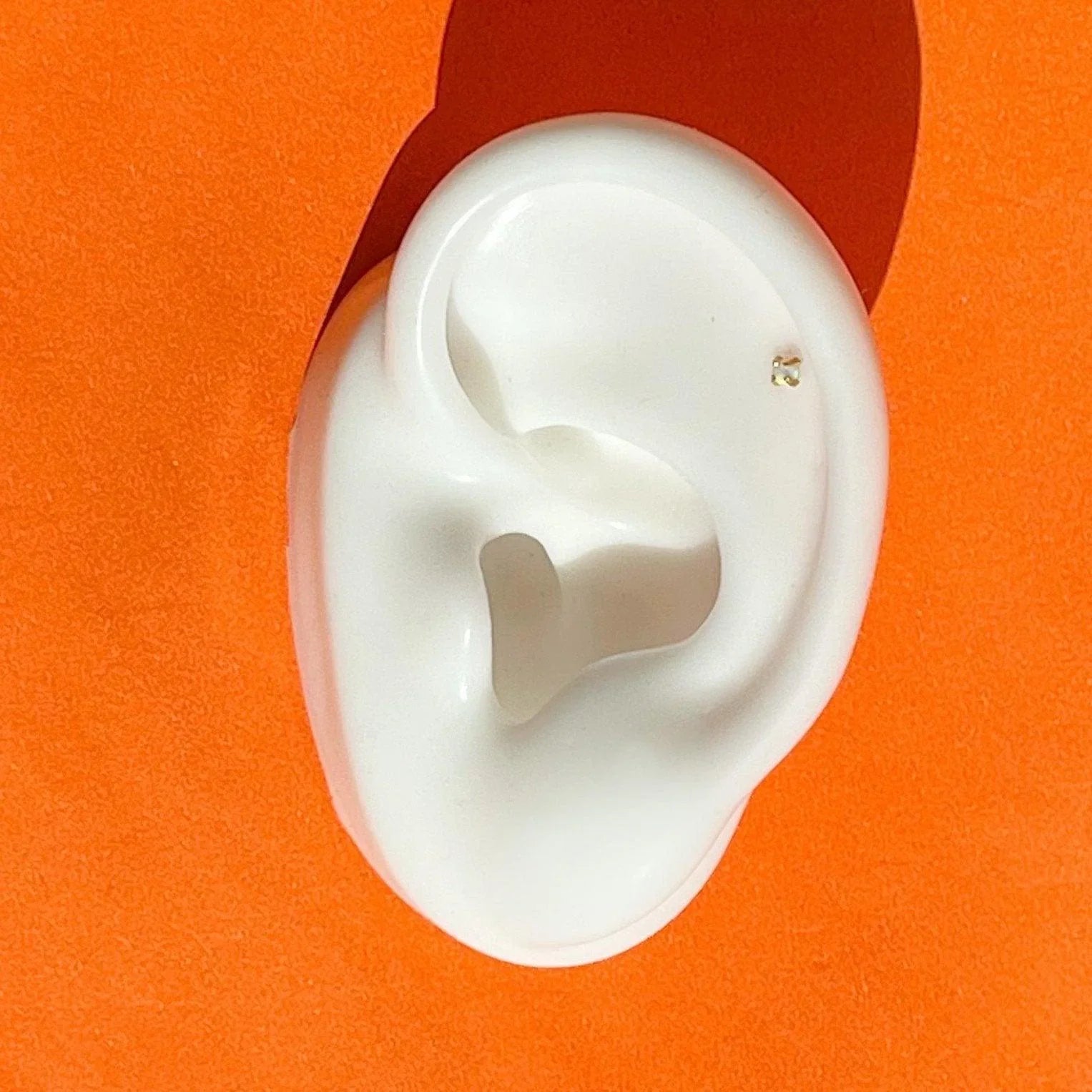 Close up of a faux ear with a tiny prong-set opal stud in a helix piercing.