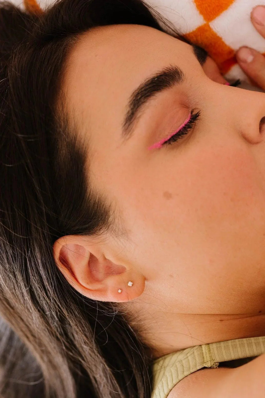Close-up of a person with pink eye makeup and two opal studs in her ear.