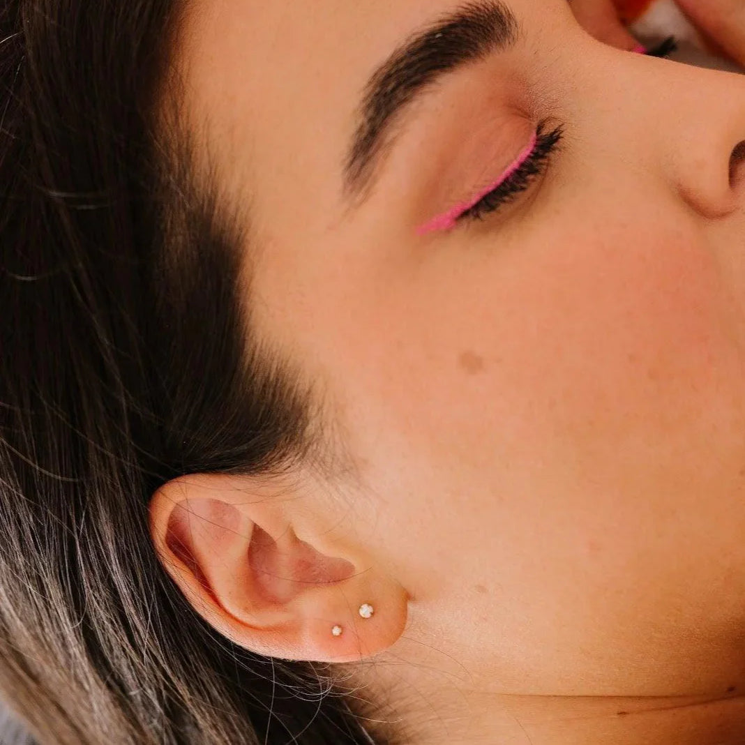 Close-up of a person with pink eye makeup and two opal studs in her ear.